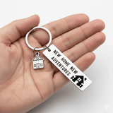 Porte-clé maison original en acier inoxydable, tenu dans une main sur fond blanc. Gravé "NEW HOME NEW ADVENTURES", idéal cadeau emménagement.