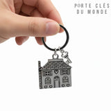 porte clé maison et clé en acier inoxydable tenu en main. Le porte-clés comporte une breloque en forme de maison, une clé sur fond blanc.