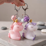 Deux porte-clés licorne avec ailes rose et mauve, tenus par leurs mousquetons avec grelots assortis