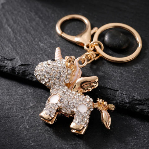 Porte clé licorne brillante doré serti de strass transparents, avec ailes, anneau et mousqueton sur fond noir