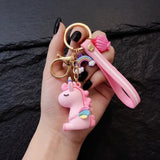 Porte clé licorne emoji rose tenu dans une main avec dragonne, arc-en-ciel et coquillage