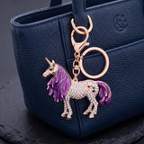 Porte clé licorne grande crinière violette serti de strass, accroché par son mousqueton à un sac bleu marine