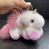 Deux porte-clés licorne en peluche rose et violet tenus en main par leurs anneaux dorés