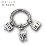 porte clé maison immobilier en acier inoxydable sur fond transparent avec 3 accessoires sur le porte clé, un panneau sold, 3 clés et une petite maison