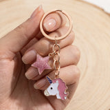 Porte-clé tête de licorne rose présenté dans une main, avec étoile rose pailletée et anneau à finition dorée rose