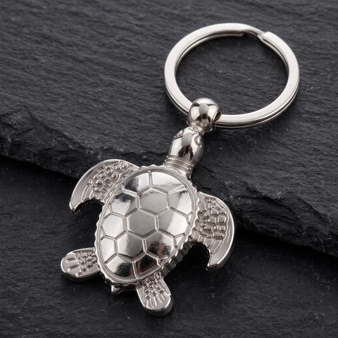 Porte clé tortue argent posé sur une surface en ardoise