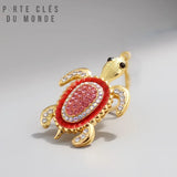 porte clé tortue avec strass rouge rubis et corps doré, sur fond blanc gris 