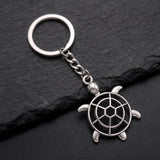 Porte clé tortue ajourée argentée avec carapace géométrique sur fond ardoise