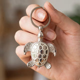 Porte clé tortue original phosphorescent en métal argenté tenu en main