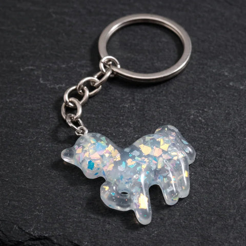 Porte clés licorne résine transparent à paillettes irisées avec chaîne et anneau métalliques, présenté sur fond noir