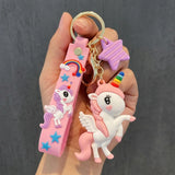 Porte-clés licorne rose pastel présenté dans une main, avec lanière à motifs licorne et arc-en-ciel et étoile violette