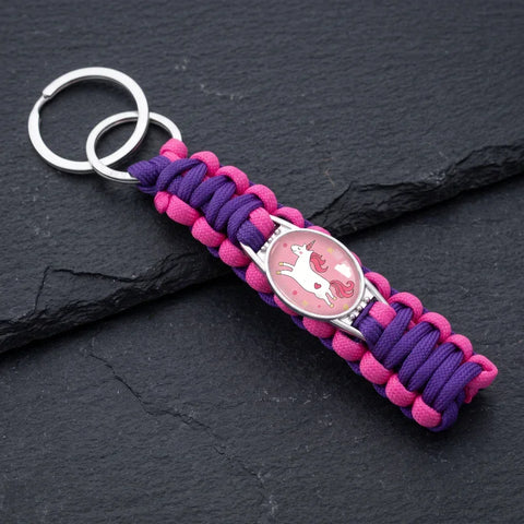 Porte clé licorne tresse violet et rose avec médaillon décoré d’une licorne, présenté sur une surface noire