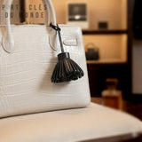 Porte clé pompon cuir noir accroché sur un sac blanc, détail élégant et raffiné pour accessoire féminin
