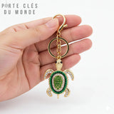 porte clés tortue avec strass verte tenu en main sur fond blanc, chaine , anneau et mousqueton doré